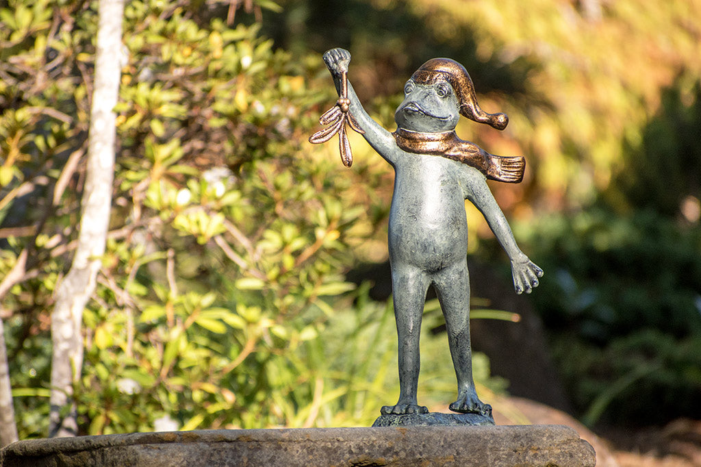 garden sculpture of frog in winter garb holding mistletoe from outstretched webbed hand