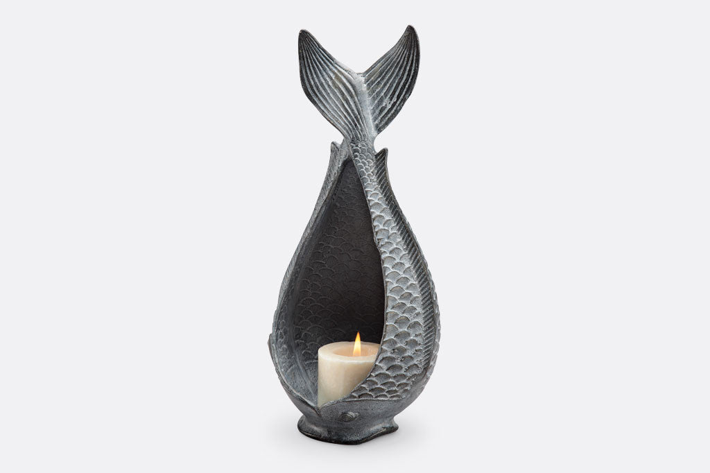 Diving Fish Candleholder shown with lit candle; fish shaped vessel with tail up in zinc; lit candle within