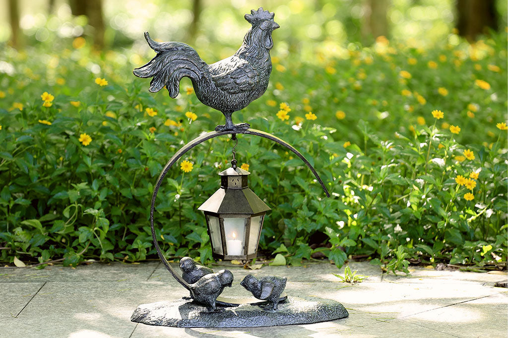 Rooster Lantern on pavement in a yard with flowers in the background