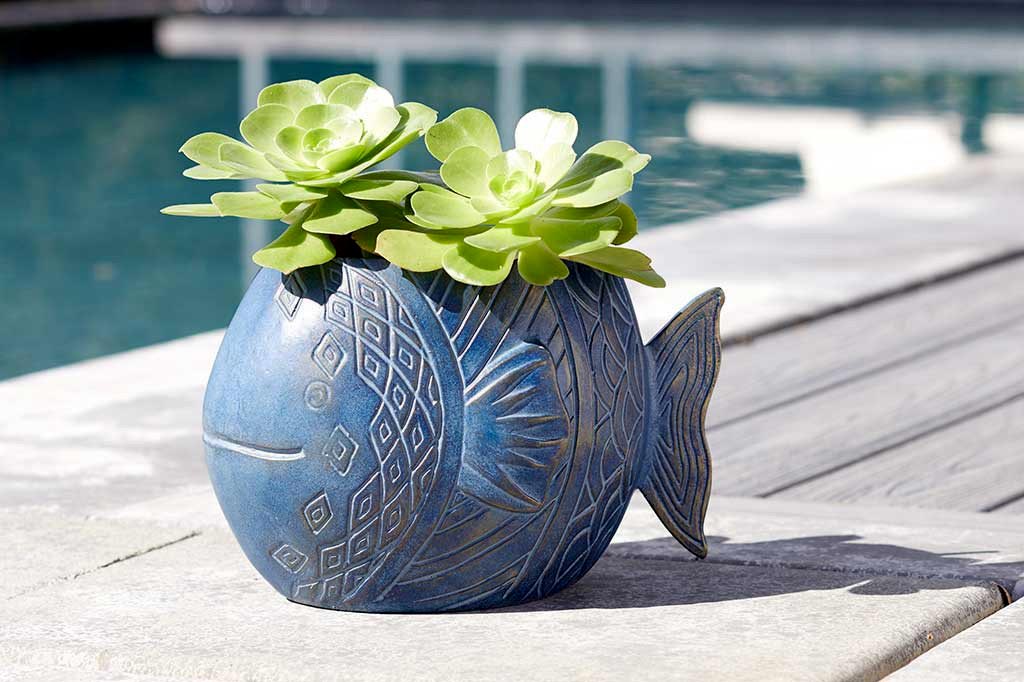 cast metal blue fish shaped planter with green succulent set by pool