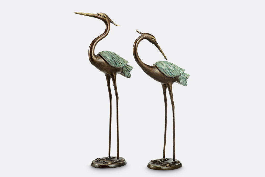 Set of two cast metal heron garden sculptures. Patina coloring on wings contrast the bronzy color of the body