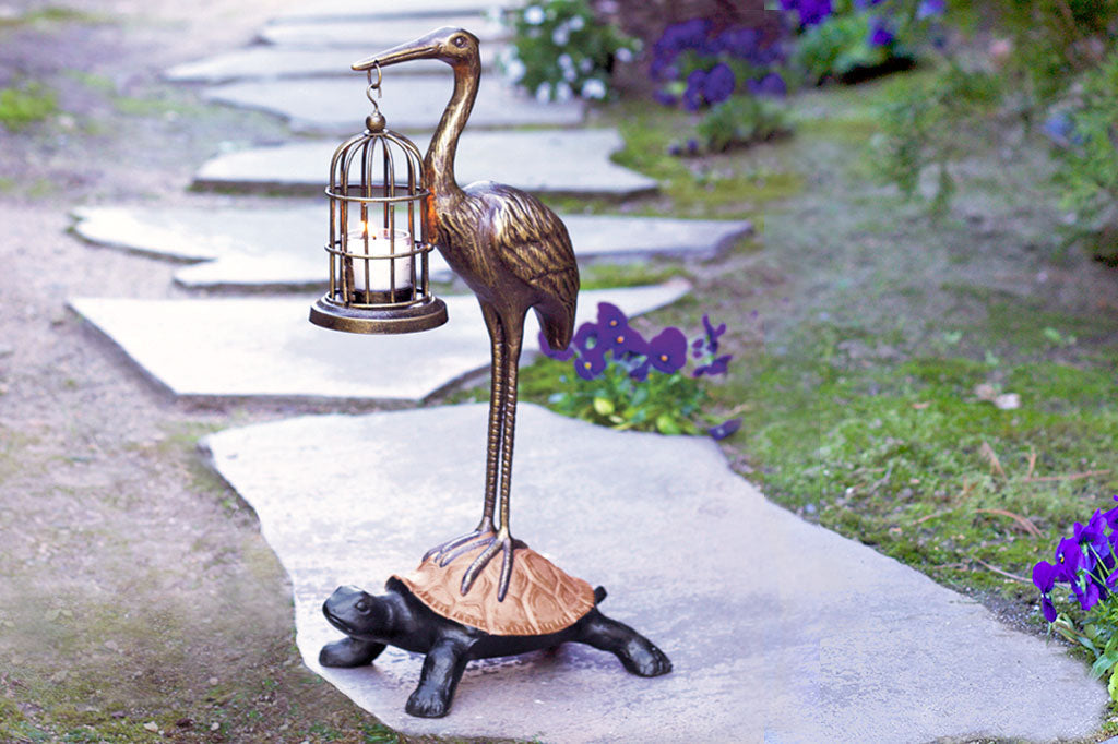 Garden sculpture of crane holding bird cage lantern, standing on a turtle's back - placed on garden path