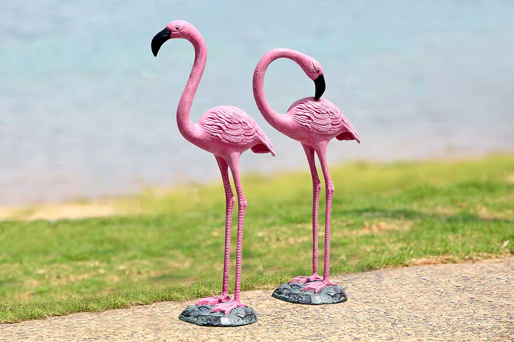 two cast metal pink flamingos on a shoreline