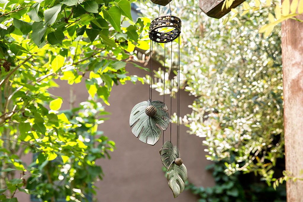 Monstera leaf windchime with circle ball knockers hanging off wooden trellis in garden setting
