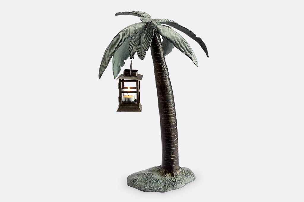 Cast metal palm tree with votive candle lantern hanging from palm leaf