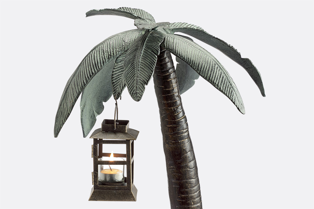 Cast metal palm tree with votive candle lantern hanging from palm leaf