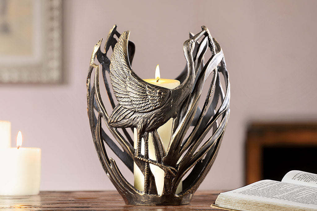 Shore bird modern sculptural candleholder shown by books on a table; holding lit pillar candle