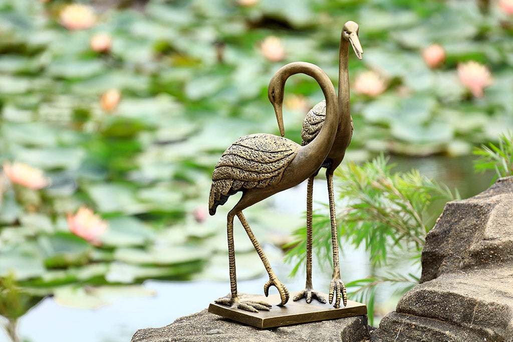 cast metal cranes on rectangle base set by lily pond