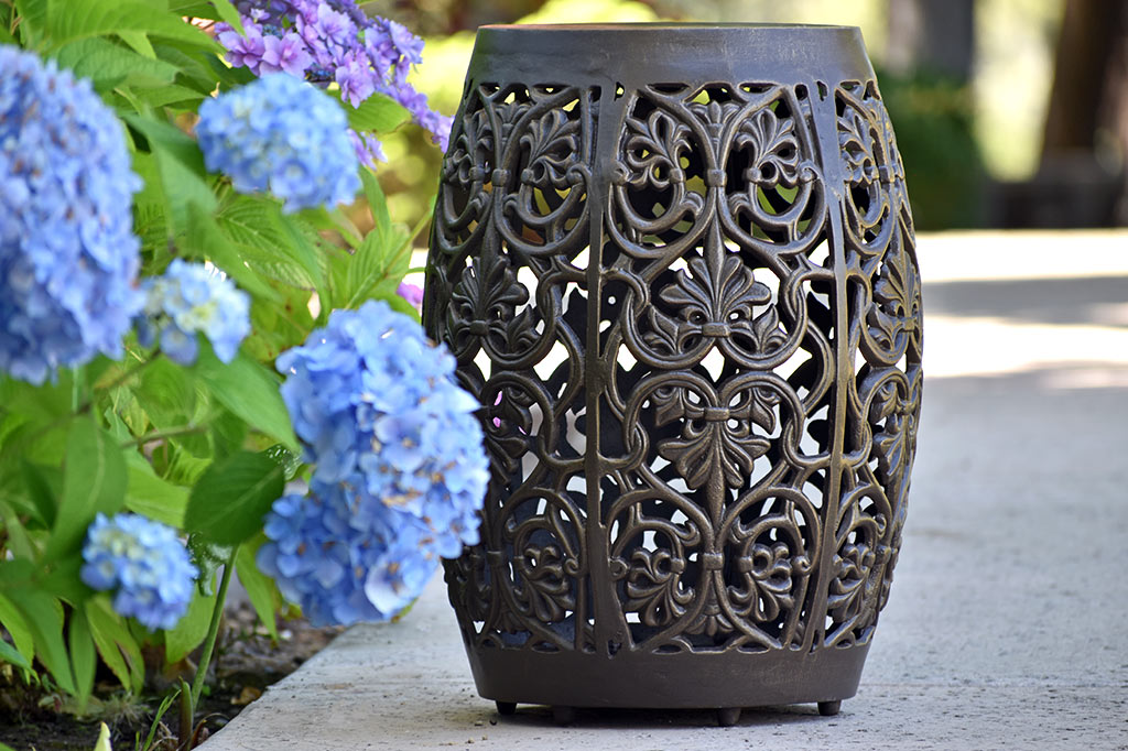 Elaborate floral scrollwork around a garden stool placed near blooming garden shrubs