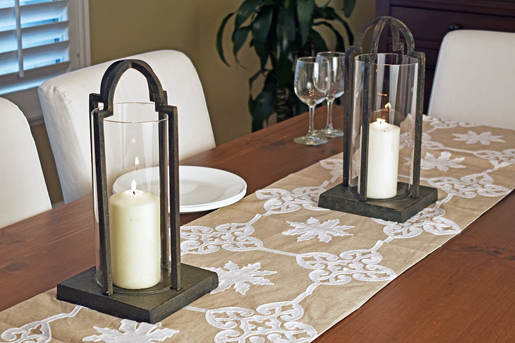 cast metal and glass lantern, geometric base holding white candle set on dining table