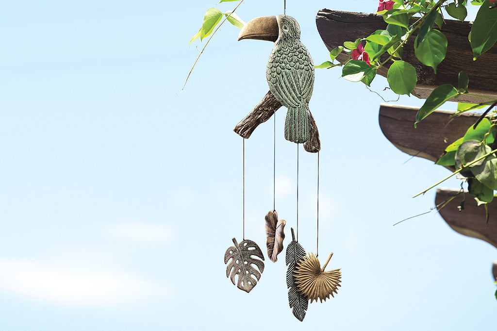 toucan windchime, pendants being tropical leaves, monstera, palm leaves. Hanging off wooden trellis