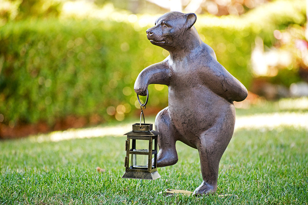 Garden bear holds lantern and picks up right foot mid-step; shown in garden on grass