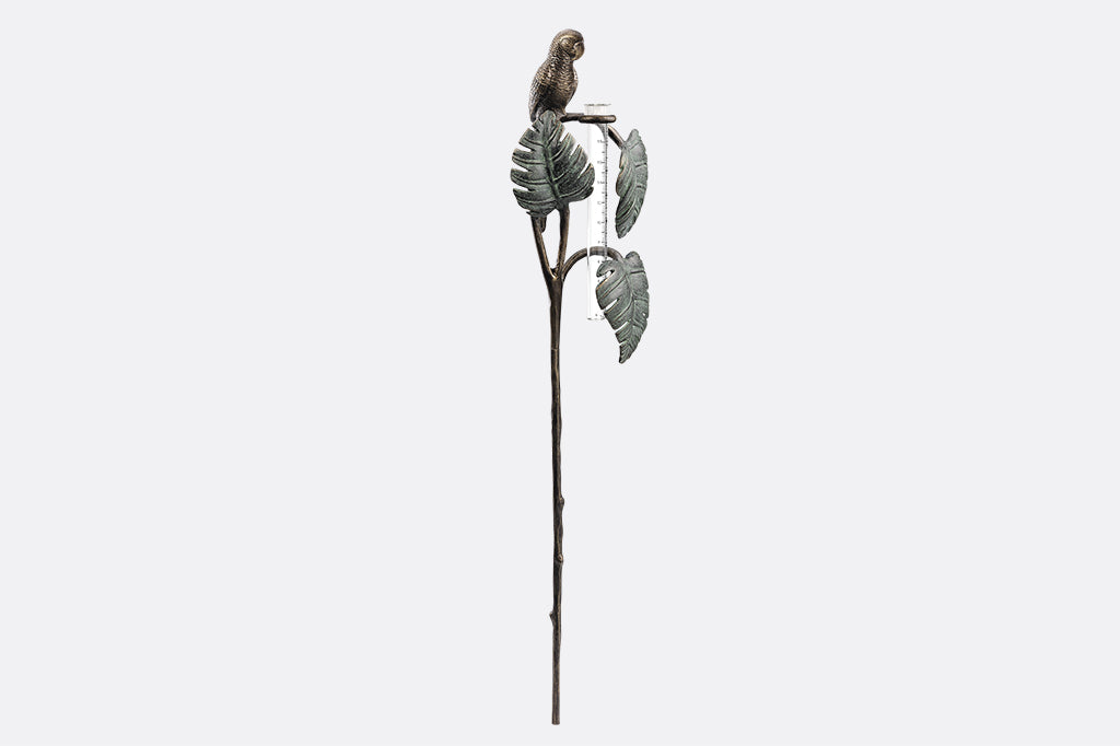 Sculptural rain catcher shaped like a Small parrot sitting on 3 tropical leaves