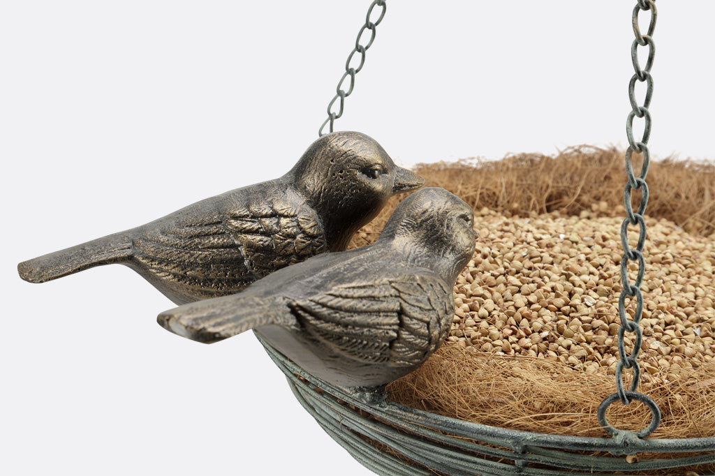Close up detail of two cast metal birds perched on edge of wire basket shaped like a nest - shown with birdseed in coco liner