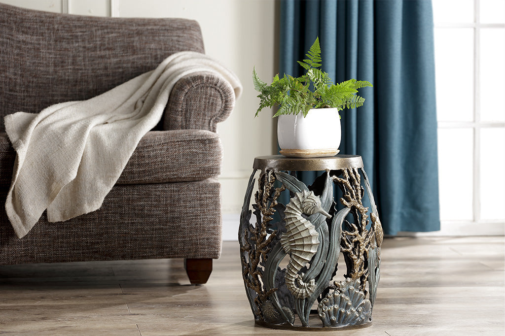 seahorse and coral theme garden stool shown in living room holding potted fern; brown couch and blue curtains in background