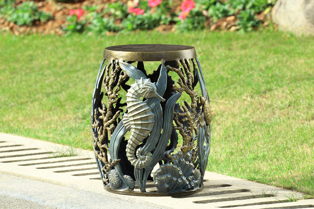 cast metal garden stool with solid seat, design of tidal animals: kelp, coral, turtle, seahorse in various finishes of green, blue, bronze, and zinc; shown on public path in garden