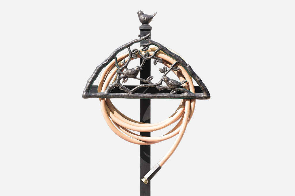 Garden staked hose holder holds ochre hose behind a decorative bird and branch screen, bird finial on stake
