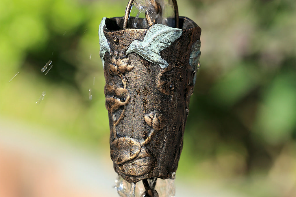 closeup view of watercup with hummingbird and leaf motif - flowing water down the rain chain