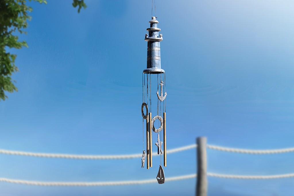 lighthouse wind chime shown near tree on sunny day; nautical theme hanging pendants: life ring, anchor, sailboat, ship wheel, seastar