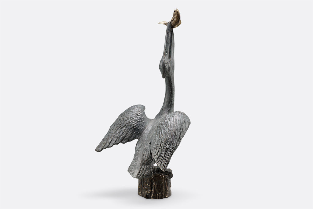 outdoor garden sculpture of heron stretching neck upwards to swallow a fish, it's perched upon top of wood pier