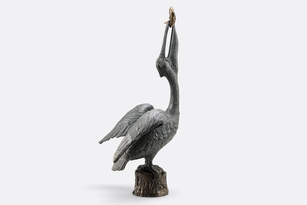 outdoor garden sculpture of heron stretching neck upwards to swallow a fish, it's perched upon top of wood pier