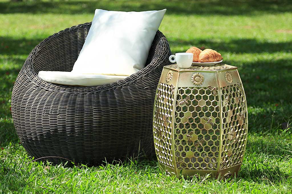 6 sided golden garden stool features honeycomb design with golden bees and sunflower medallions - shown by outdoor papasan on a lawn, food on top of stool