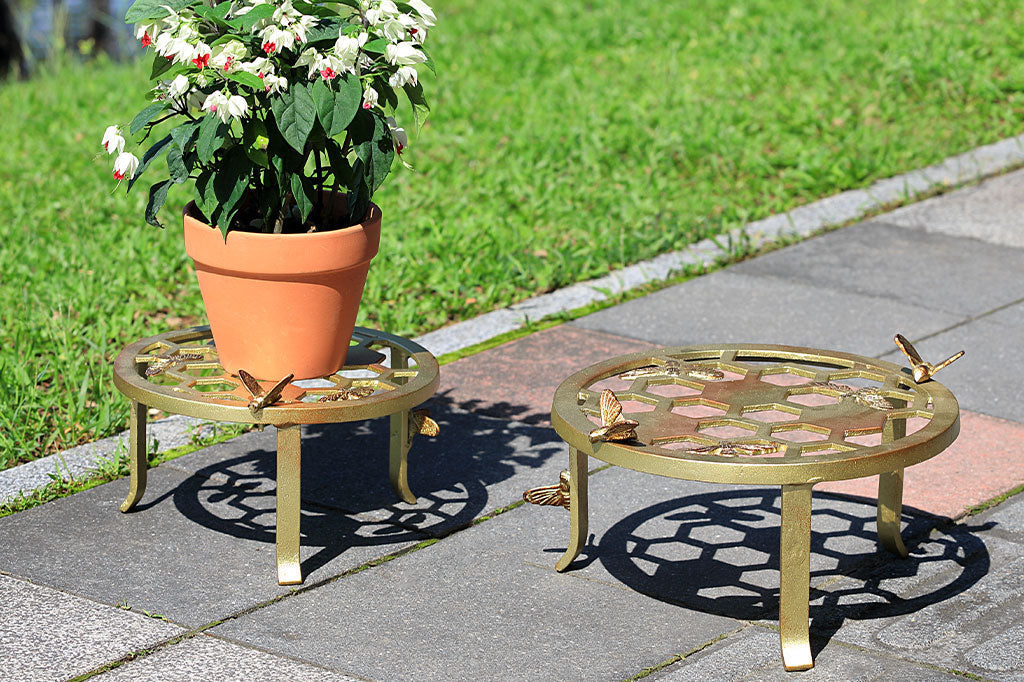 Two plant stands showing honeycomb and bee motif, one large and one small. Small one holds potted plant - both are outside near lawn