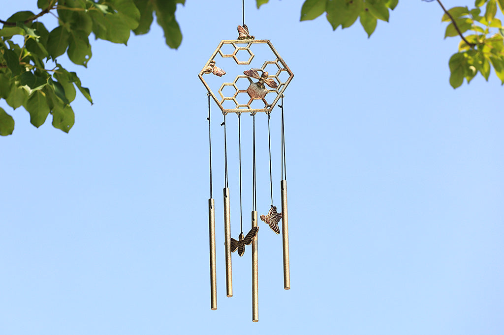 Wind art showing honeycomb and bee motif is hanging under tree on sunny day