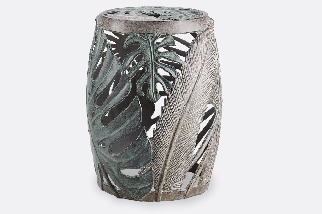 Las Palmas Garden Stool is adorned on all sides with a variety of hand sculpted tropical leaves. The leaves on this stool have been finished in verdigris and bronze over cast aluminum.