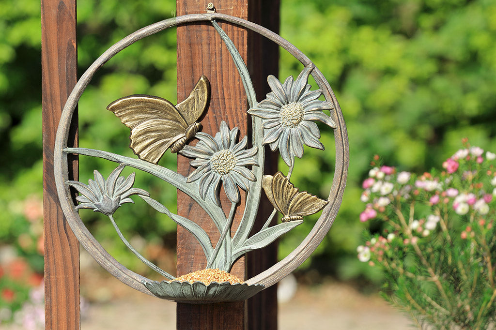 hanging bird feeder station featuring butterflies and daisies, mounted to a porch railing with plants in the background