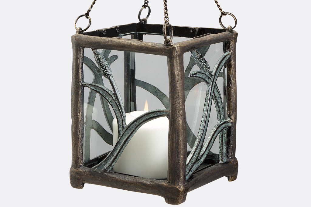 close up view of hanging candle lantern with cattail motif. Lit candle inside.