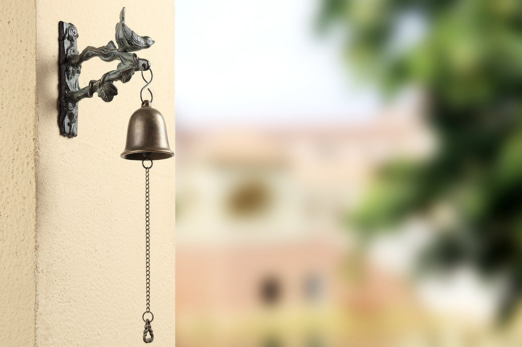 Songbird Mounted Wind Bell on outdoor wall of house with trees in the background