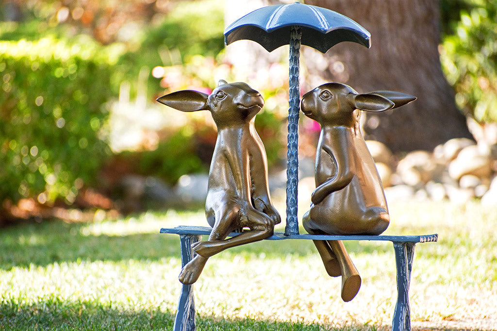 cast metal sculpture with two bunnies sitting under a umbrella