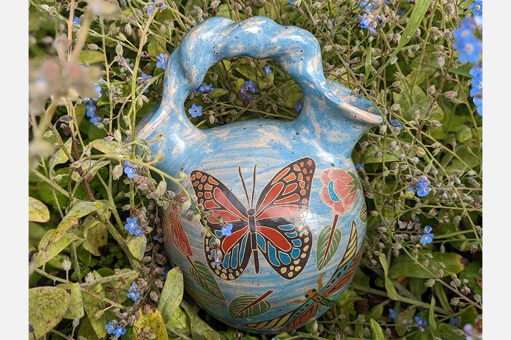 blue vase with two openings and a roped handle, hand etched nature designs, large butterfly in center. Placed in garden