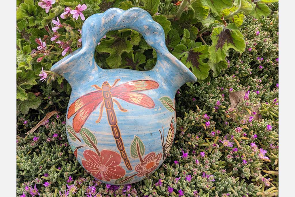 blue vase with two openings and a roped handle, hand etched nature designs, large dragonfly in center. Placed in garden