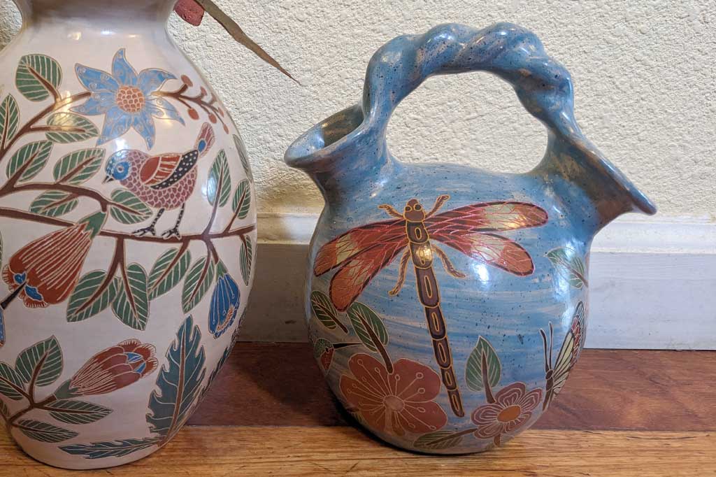 blue vase with two openings and a roped handle, hand etched nature designs, large butterfly in center. Placed in garden