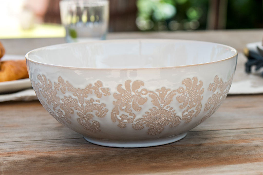 White ceramic vessel with blush on white, lace-inspired embossed design shown on a wide bowl in a dining table setting