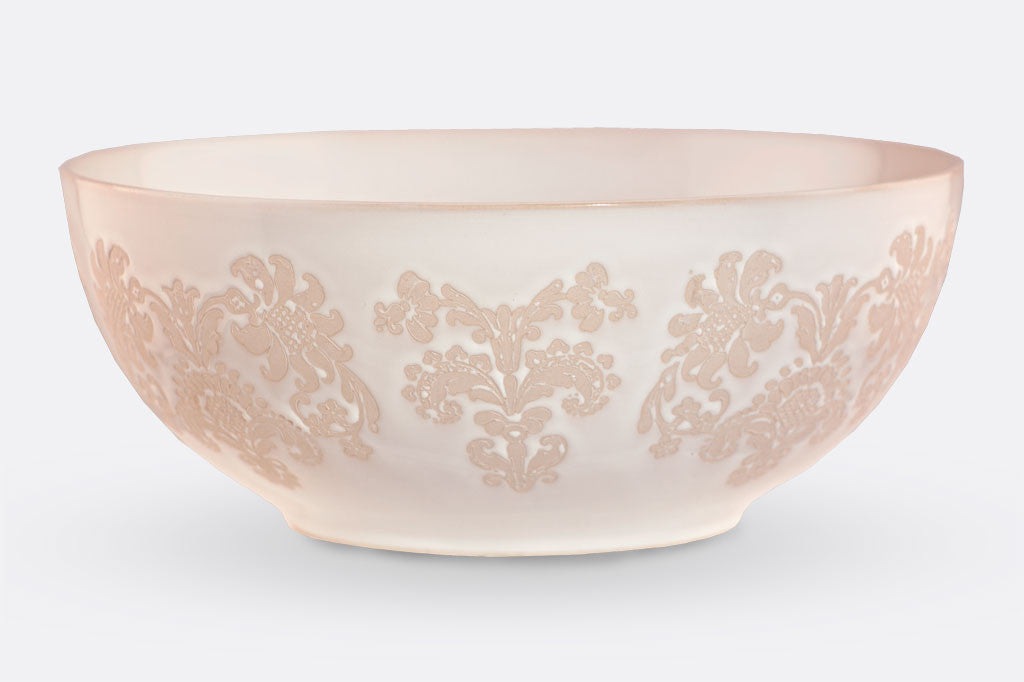 White ceramic vessel with blush on white, lace-inspired embossed design shown on a wide bowl.