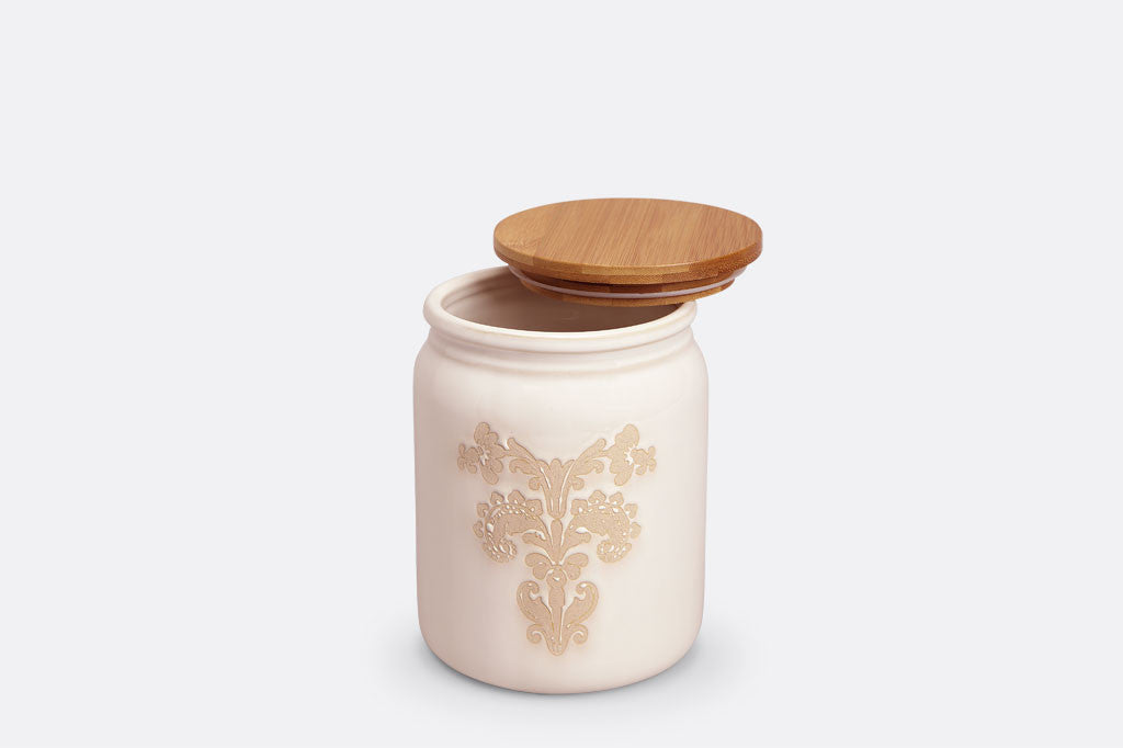 White ceramic vessel with blush on white, lace-inspired embossed design shown on canister with bamboo lid, lid slightly ajar shows rubber seal