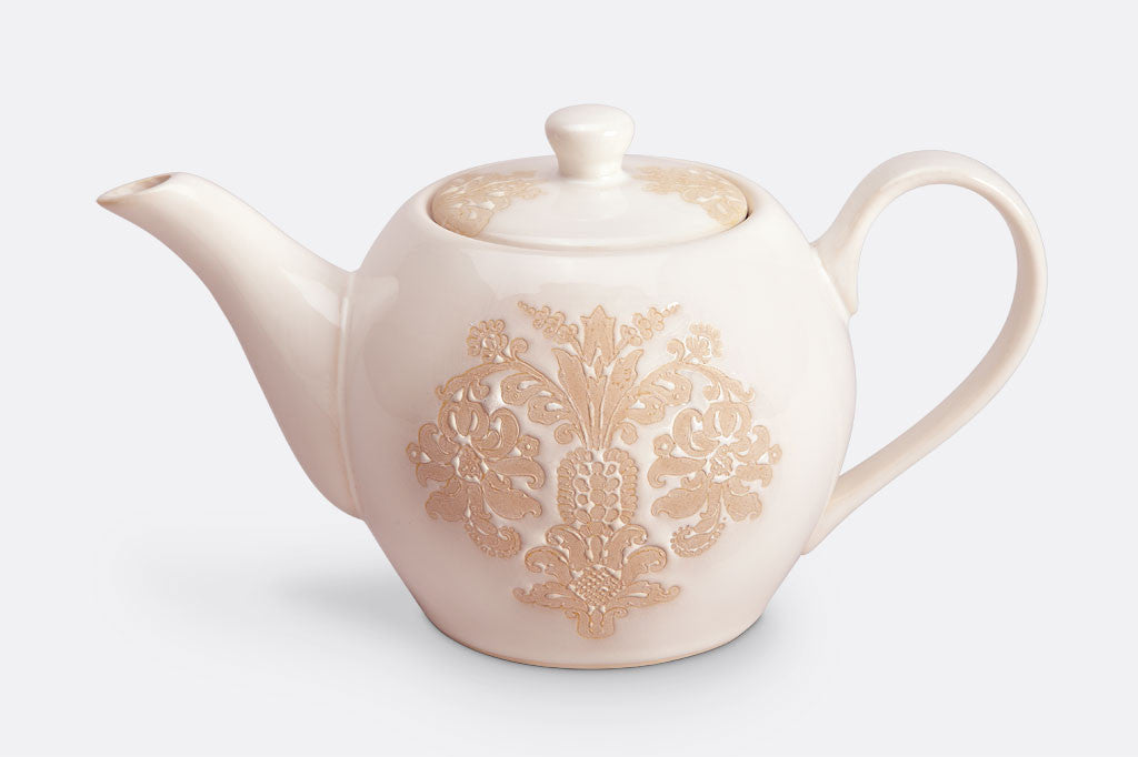 White ceramic vessel with blush on white, lace-inspired embossed design shown on a teapot.