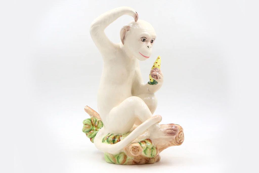 cream colored ceramic monkey scratching its head and holding a fruit