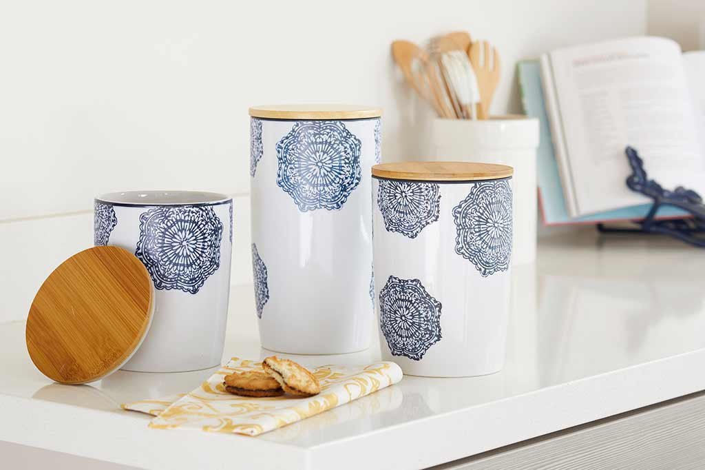 3 sizes of canister shown in kitchen: canisters of white ceramic with blue mediterranean glazed print and blue rim; has wood lid