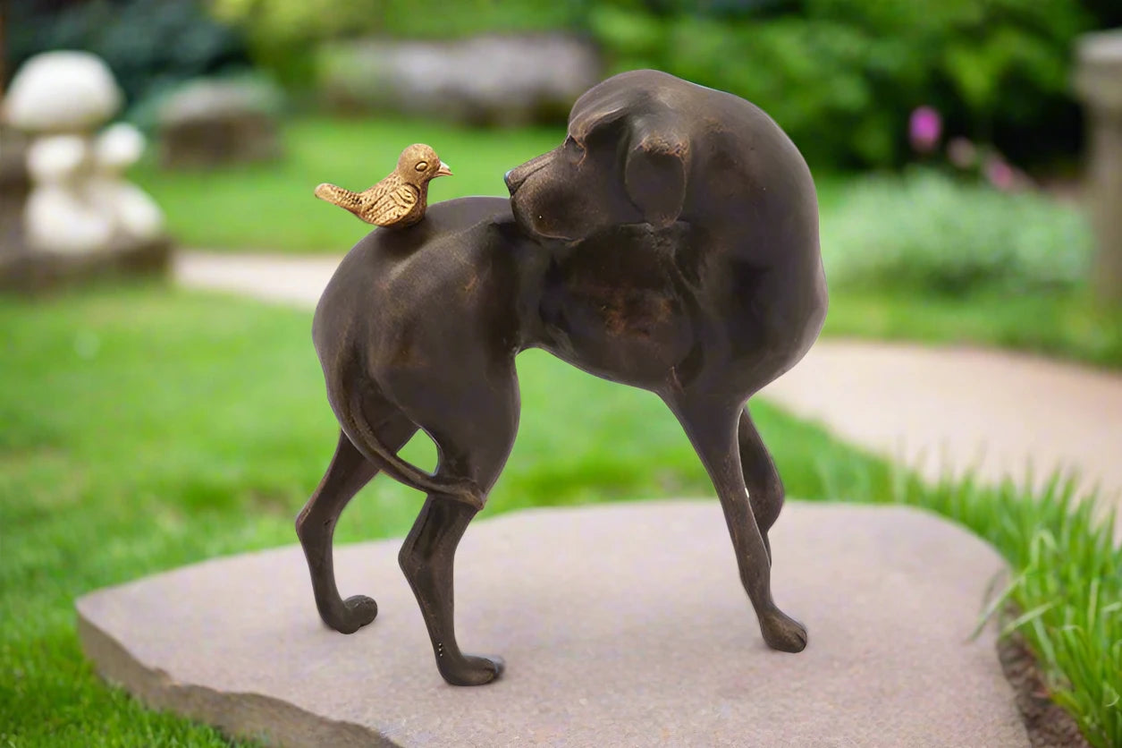 cast metal garden sculpture of dog looking at a bird on its back