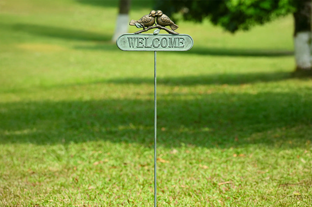 Staked metal welcome sign in verdi with two bronze birds on a branch perched above the sign