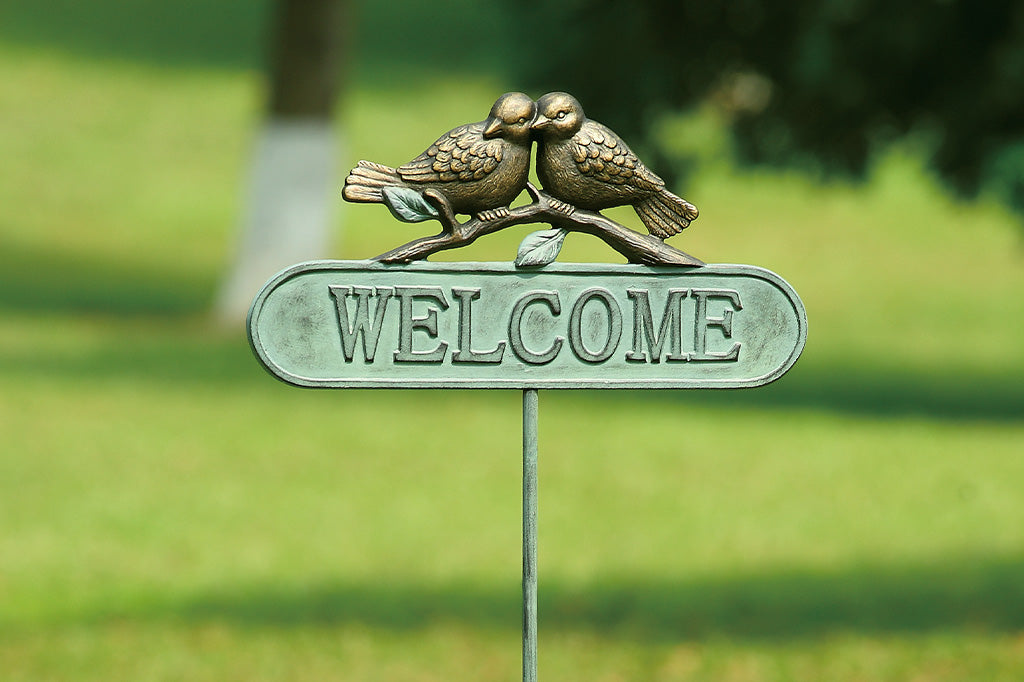 Staked metal welcome sign in verdi with two bronze birds on a branch perched above the sign