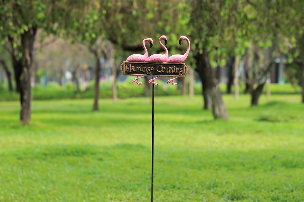 cast metal staked lawn sign reading "flamingo crossing" with three pink flamingos. placed in lawn 