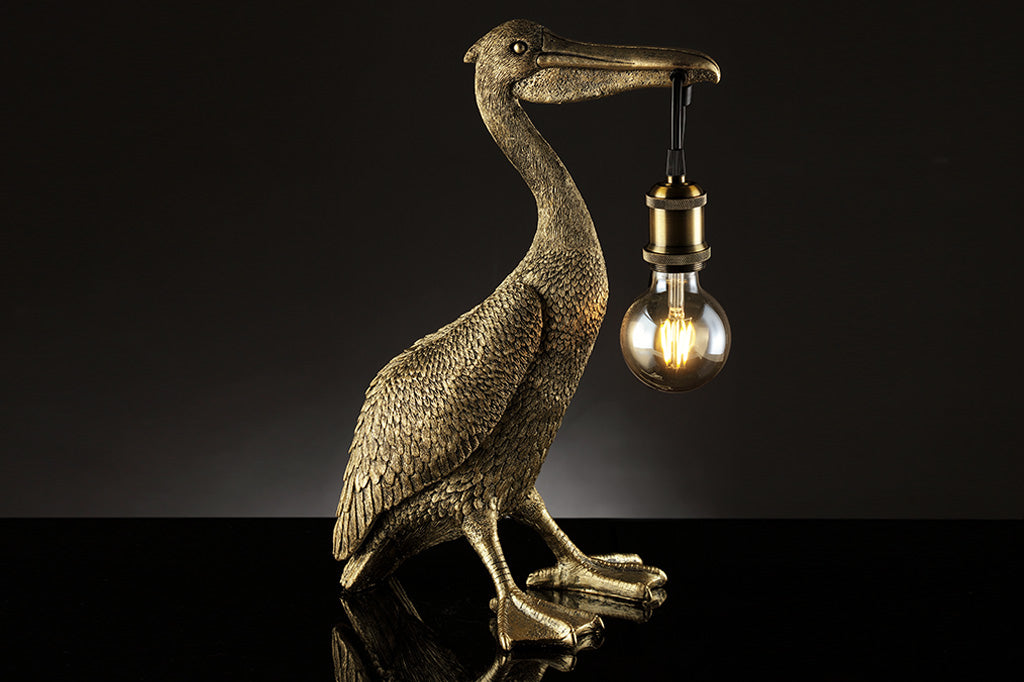 novelty desk lamp of pelican holding lightbulb by the beak - gold finished resin, shown in dark studio 