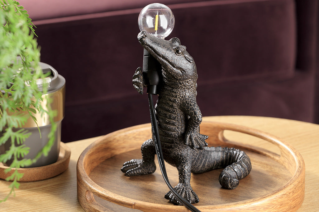 novelty desk lamp, resin alligator holding lightbulb shown on coffee table in living room by houseplant