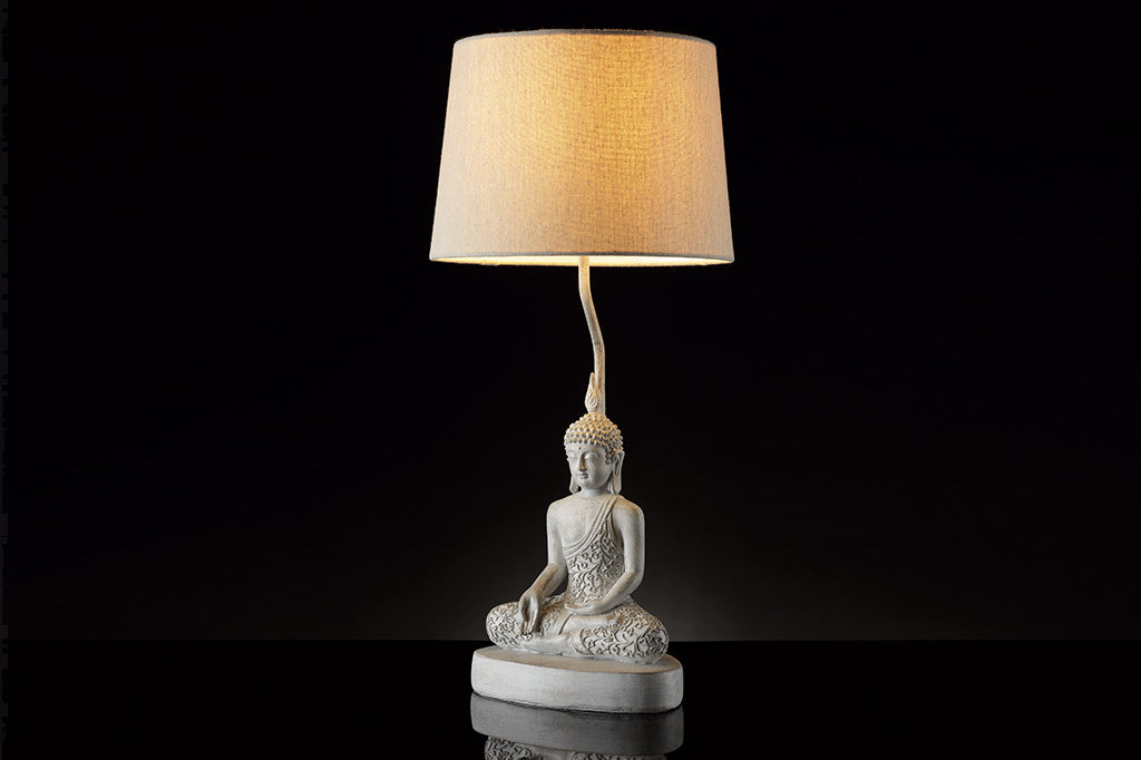 cream colored Resin Buddha sculpture table lamp with cream fabric shade shown in black studio setting