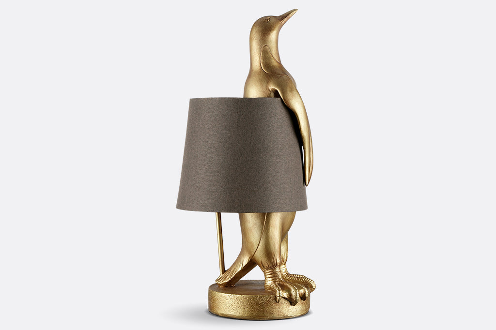 face right view of whimsical table lamp of gold finished resin penguin wearing a brown fabric lampshade around its torso.